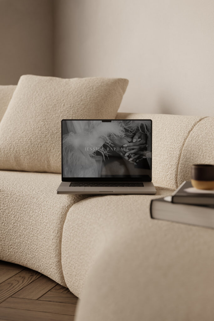 Laptop on a cosy sofa showing a black and white wedding photograph with the Jessica Raphael Photography logo over it.